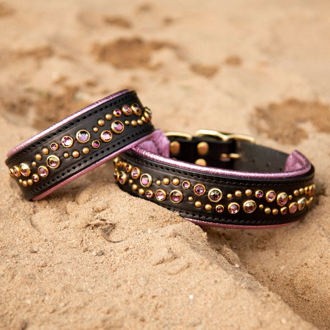 Two black leather dog collars with amethyst crystals on a sandy surface