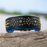 Black leather dog collar with blue crystals, brass hardware and metallic blue padding on a stone.