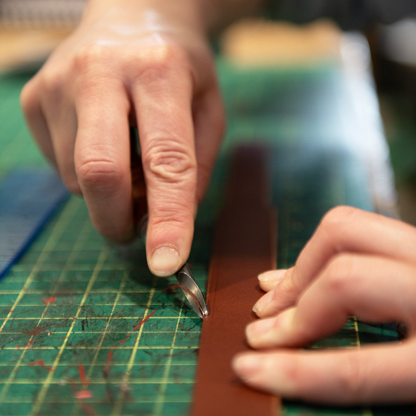 Close-up of a person's hands using an edge beveler to bevel a  strip of leather for a custom dog collar, on a green gridded cutting mat.