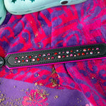 Black leather dog collar with red and pink gemstones on a colorful beach towel.