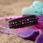 Black leather dog collar with pink stones on a towel on a sandy surface
