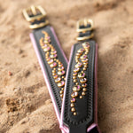 Black leather Dog Collars with pink crystals laid flat on a beach