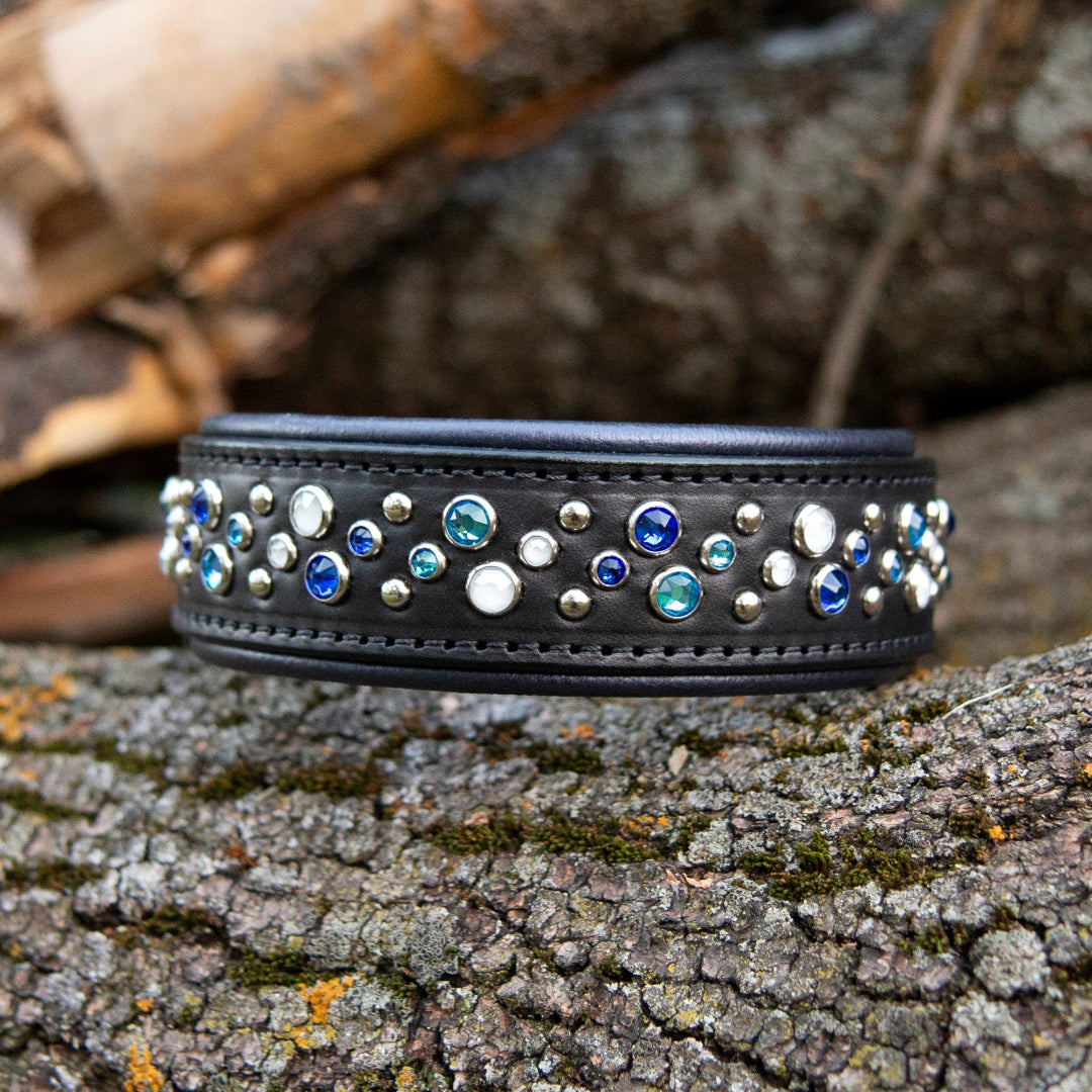 Black leather dog collar with blue and white crystals on a log