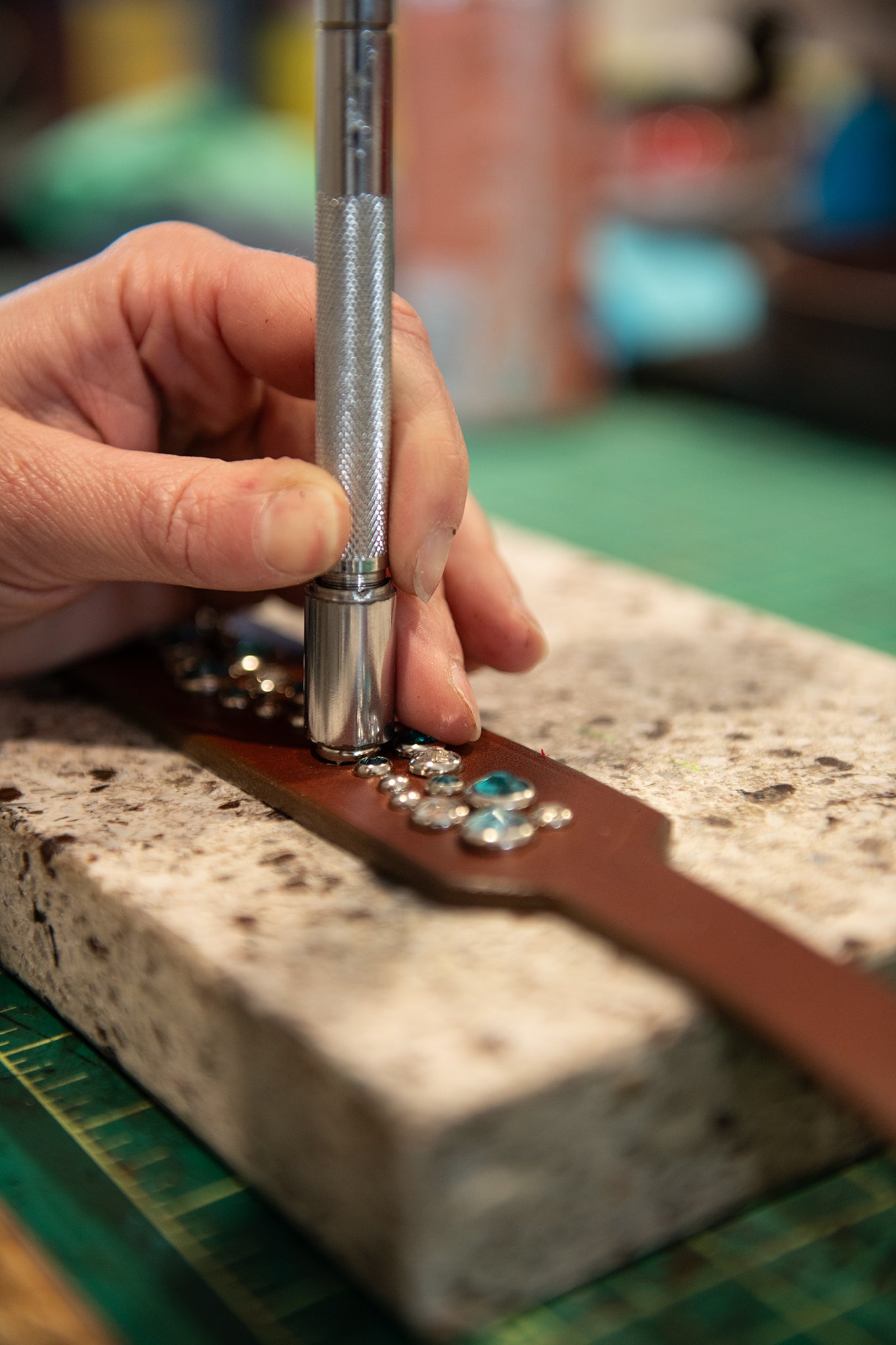 Hand using a tool on a leather strap with decorative elements on a stone surface.